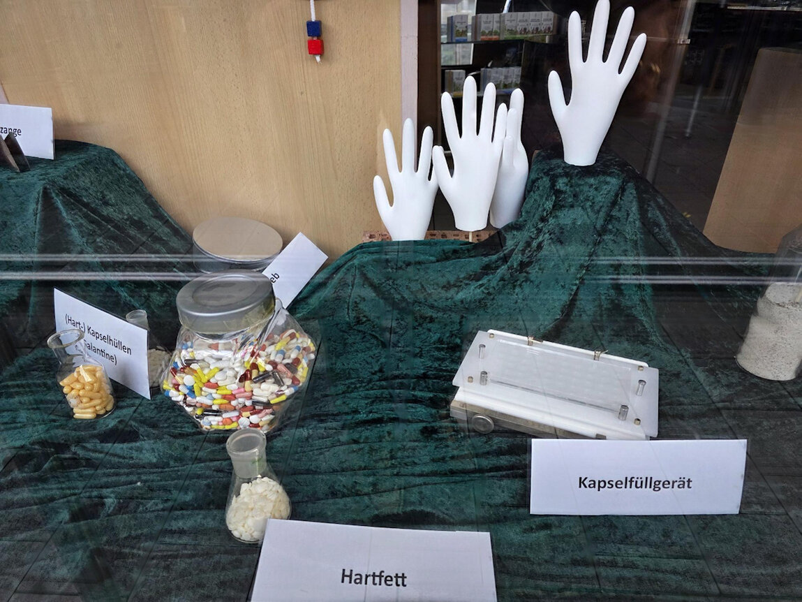 Dekoration im Schaufenster mit weissen Händen, Erklärungen auf Schildern und Pillenbox